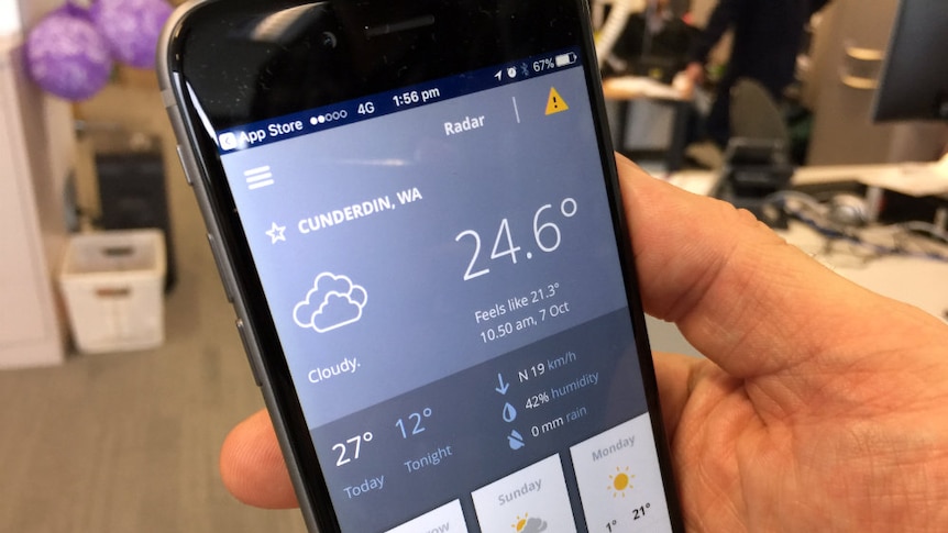 Weather information is displayed on a smartphone held in a man's hand