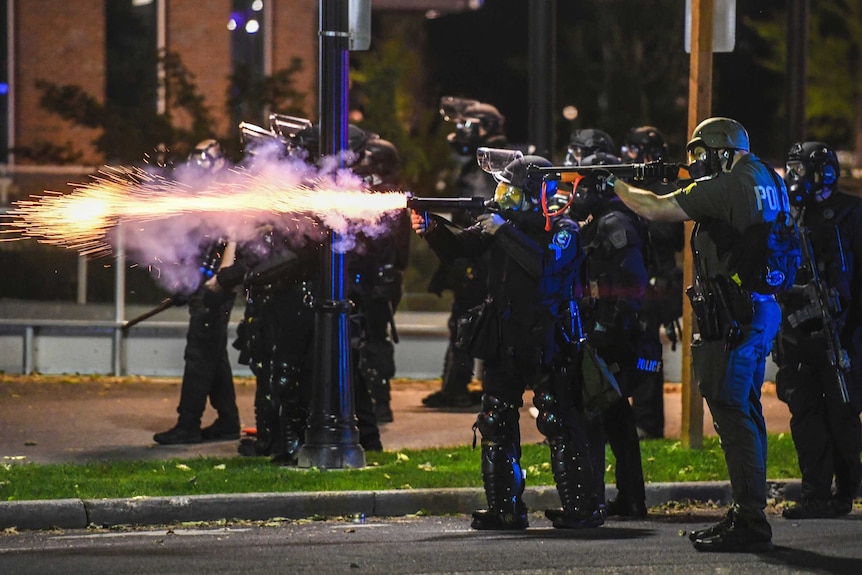 Police in riot gear with flames shooting out of a gun