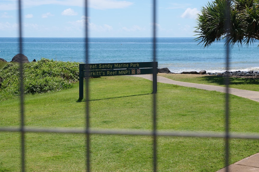 A photo through a temporary work fence shows a sign that marks the start of the Great Sandy Marine Park. 