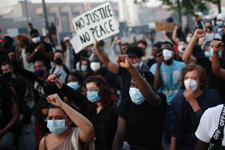 Protesters wearing face masks hold posters and raise their fists during a demonstration.