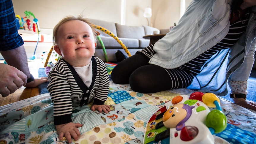 Oskar crawling on his play mat while looking up and flanked by his parents.