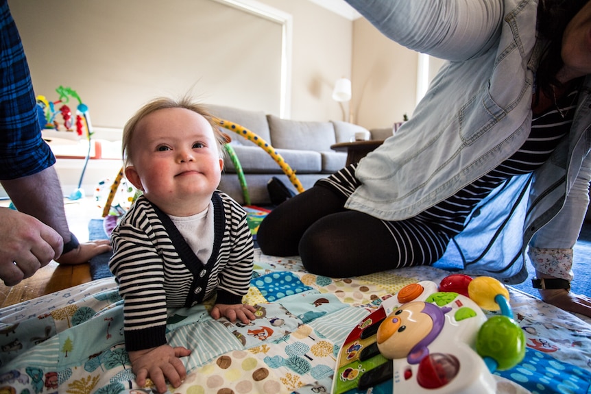 Oskar crawling on his play mat while looking up and flanked by his parents.