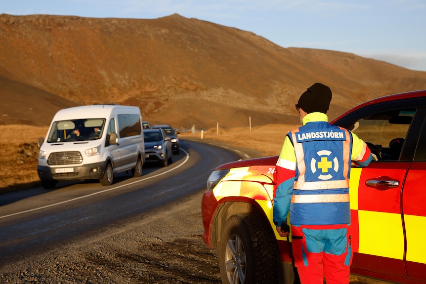 A destra è raffigurato un membro dei servizi di emergenza con indumenti ad alta visibilità mentre un grande camion bianco avanza verso di lui.