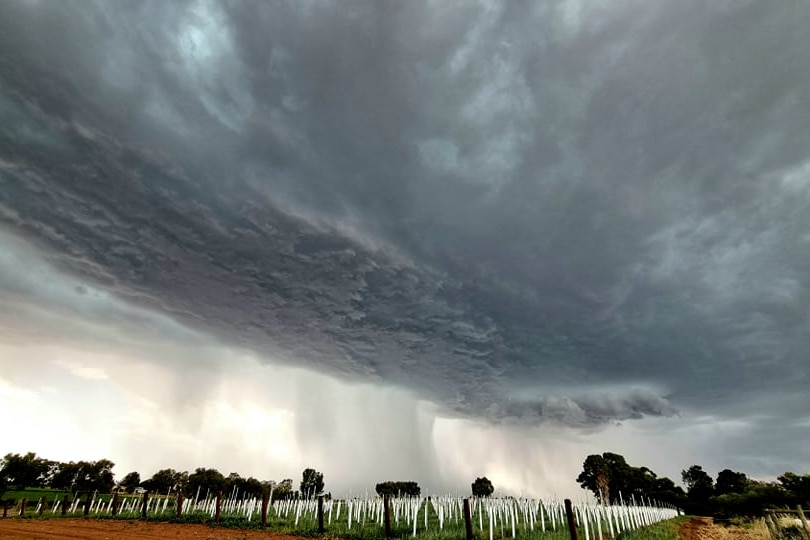 Dark and threatening storm clouds hang over a rural scene at dusk