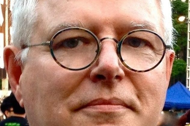 A man with white hair wears thick framed eye-glasses and purses his lips as he stares into the camera in hong kong