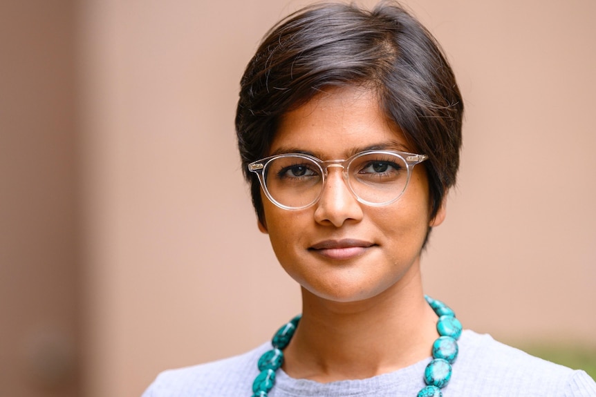 A woman wearing glasses appears in a professional portrait