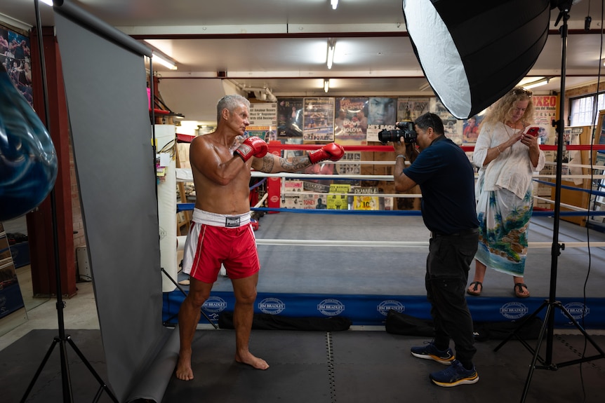 McBride shirtless and wearing boxing gloves, poses for a photographer in front of a boxing ring.