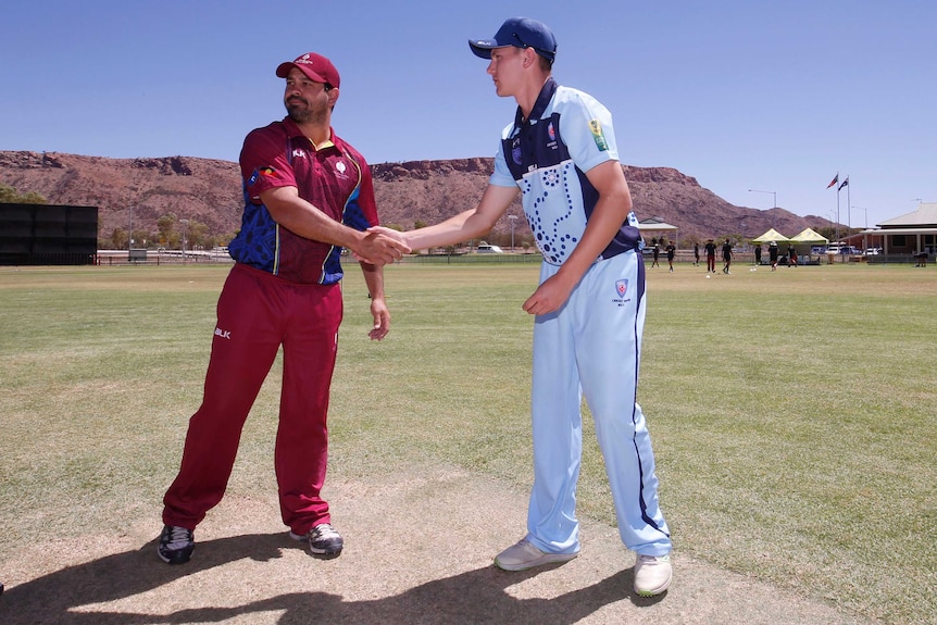 Two cricketers shake hands on the field.