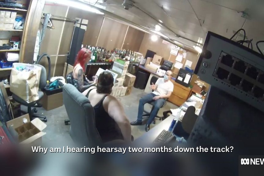 CCTV vision shows man sitting down talking to two women in an office.