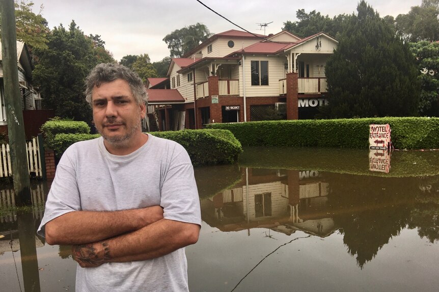A man stands with arms crossed in front of his flooded motel.