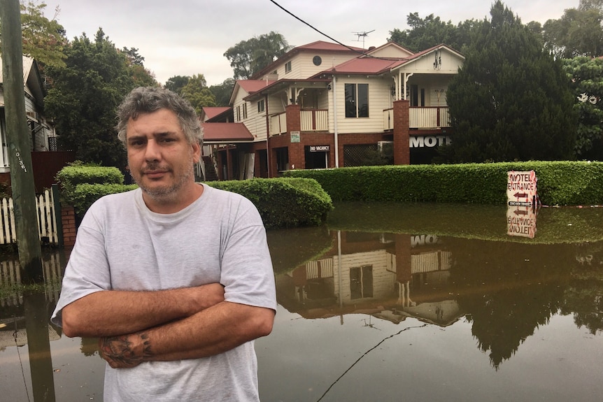 A man stands with arms crossed in front of his flooded motel.