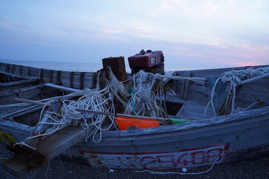 The wreck of a North Korean wooden boat with tangled ropes washed ashore on a beach.