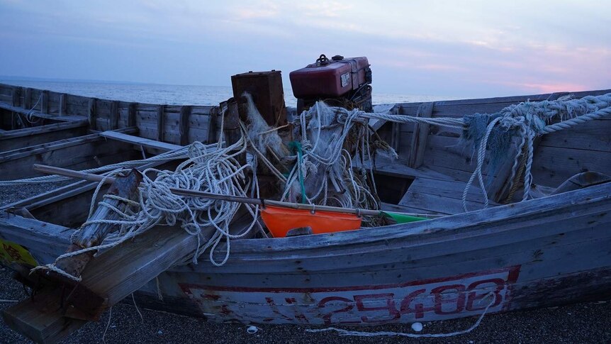 The wreck of a North Korean wooden boat with tangled ropes washed ashore on a beach.