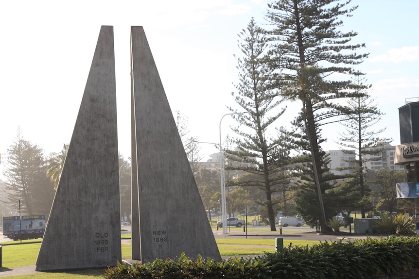 Two triangular cement structures with QLD and NSW engraved, trees and cars in background