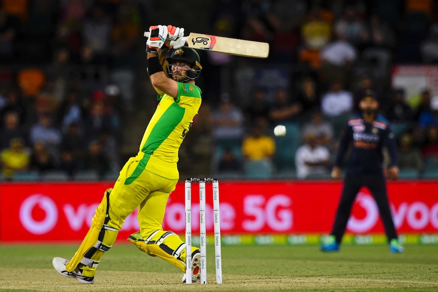 An Australian male batter looks over his shoulder as he watches a ball he hit.