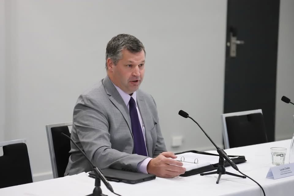  table efore a microphoneA man in a grey suit sits at at