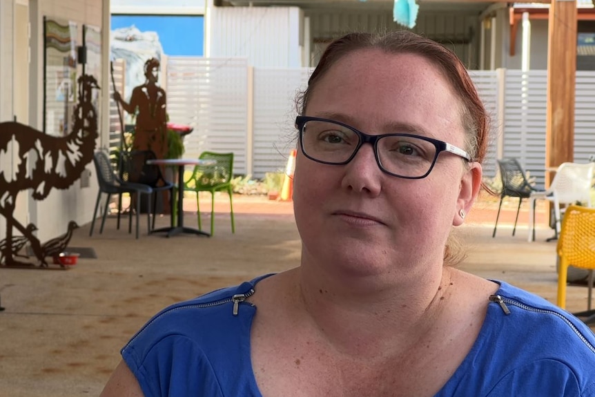 She wears a blue shirt and stands in the shade near tin statues