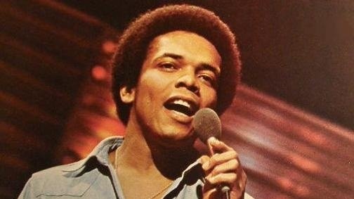 Johnny Nash in his youth, performing on stage, holding a microphone.