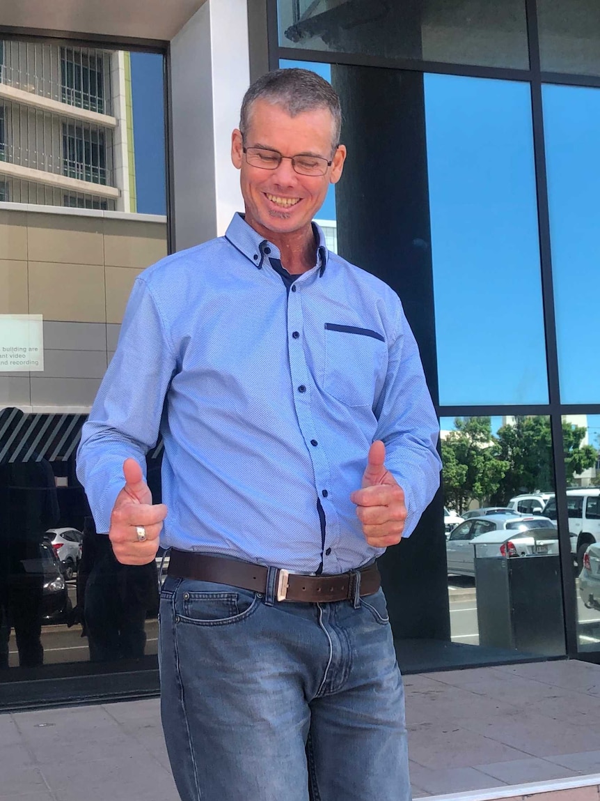 A man walking down stairs from a courthouse with his thumbs up.