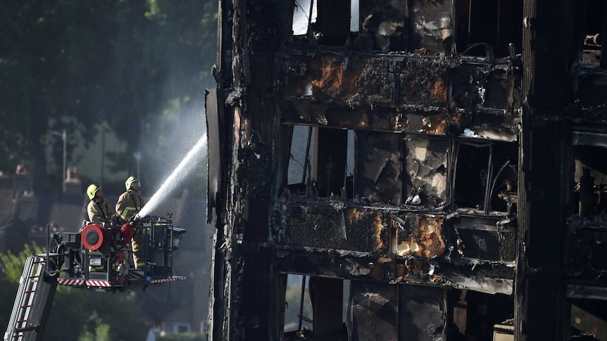 Firefighters spray water onto the Grenfell Tower block which is blackened and decaying from a fire.