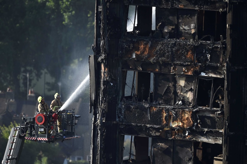 Firefighters spray water onto the Grenfell Tower block which is blackened and decaying from a fire.