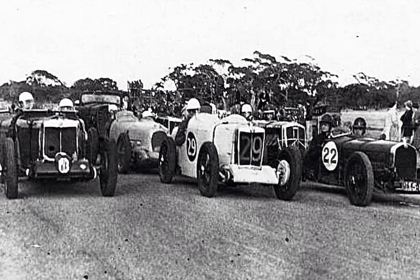 A black and white photograph of 1930s racing cars with their drivers waiting to start