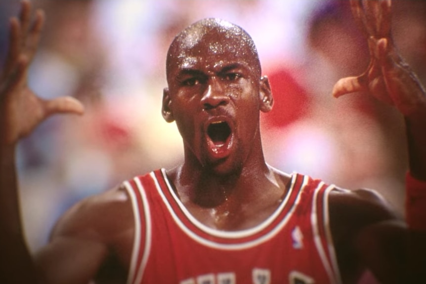 A sweat-soaked Michael Jordan stands, mouth agape, hands high, while playing for the Chicago Bulls.