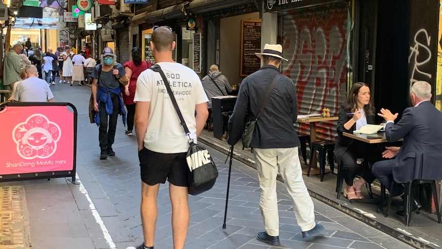 People walk down a Melbourne laneway, while others dine at outdoor tables nearby.