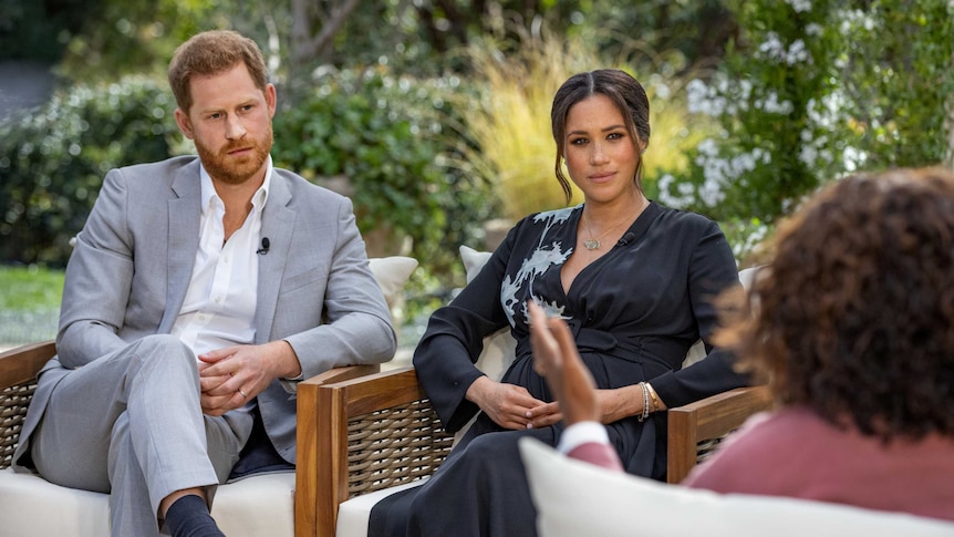 Prince Harry and Meghan Markle sitting in chairs in a garden facing Oprah Winfrey