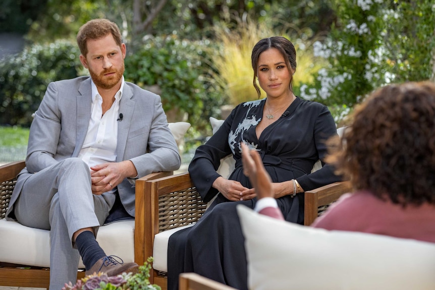 Prince Harry and Meghan Markle sitting in chairs in a garden facing Oprah Winfrey