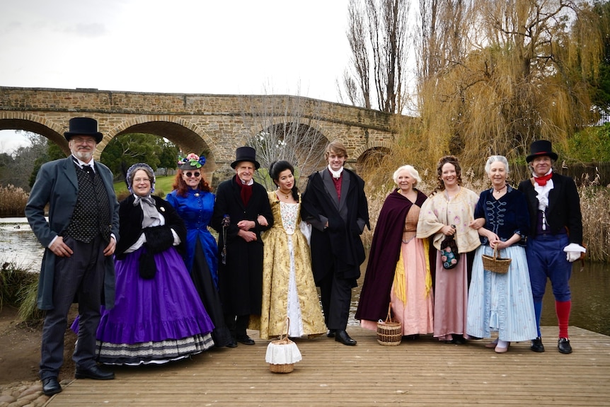 A group of people in historical outfits stand in front of the convict-era Richmond Bridge.