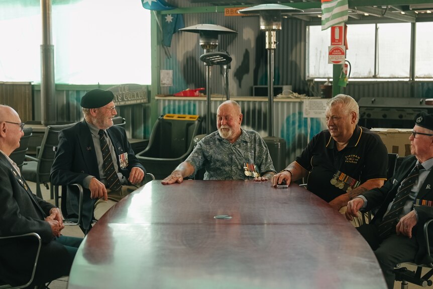 Five older men sit around a table.