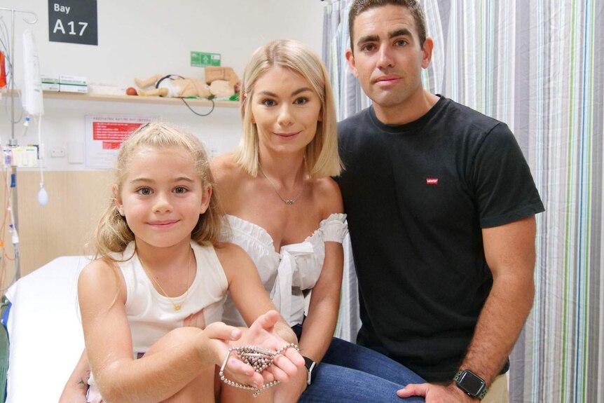 Seven-year-old Olivia Fay sits on bed with her parents in a medical clinic.