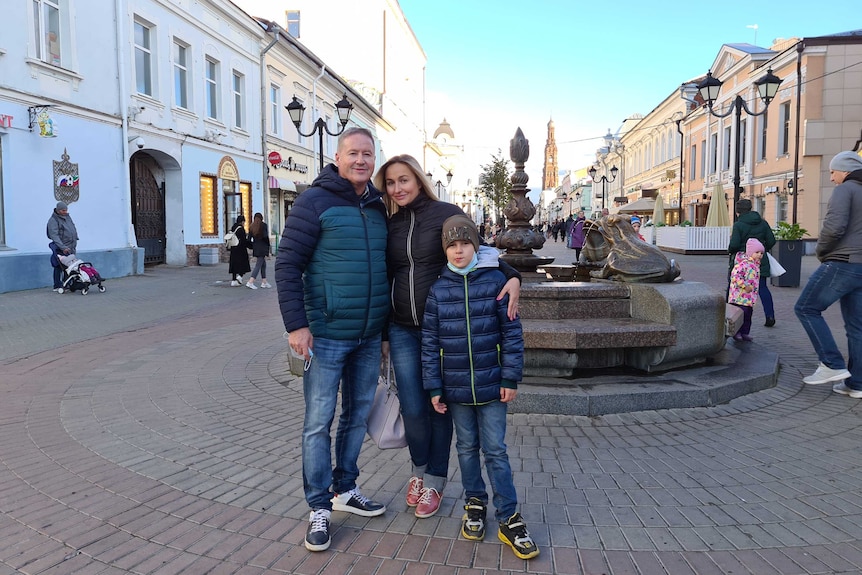 Adrian Lister with his partner and her son standing in front of a fountain in a public square in Kazan