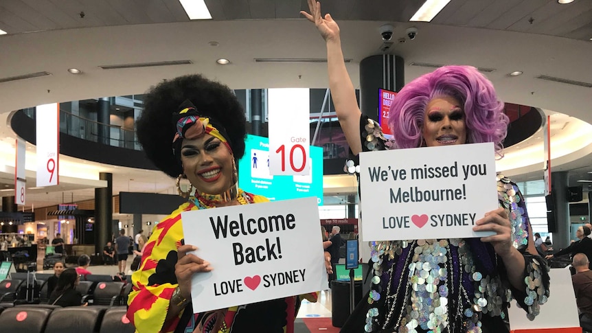 Two girls stand other side of pilot with signs that read "We've missed you Melbourne"