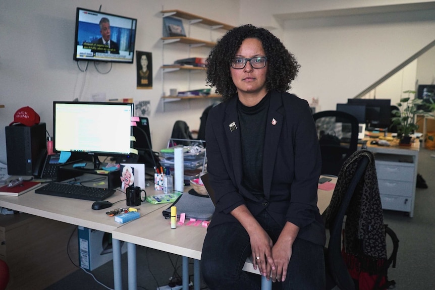 Mandu Reid sits on a desk in her office and looks at the camera.