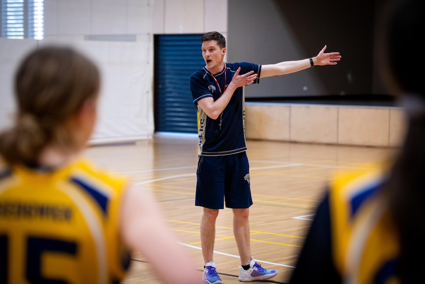 A man with a whistle on a basketball court, motioning to the side.