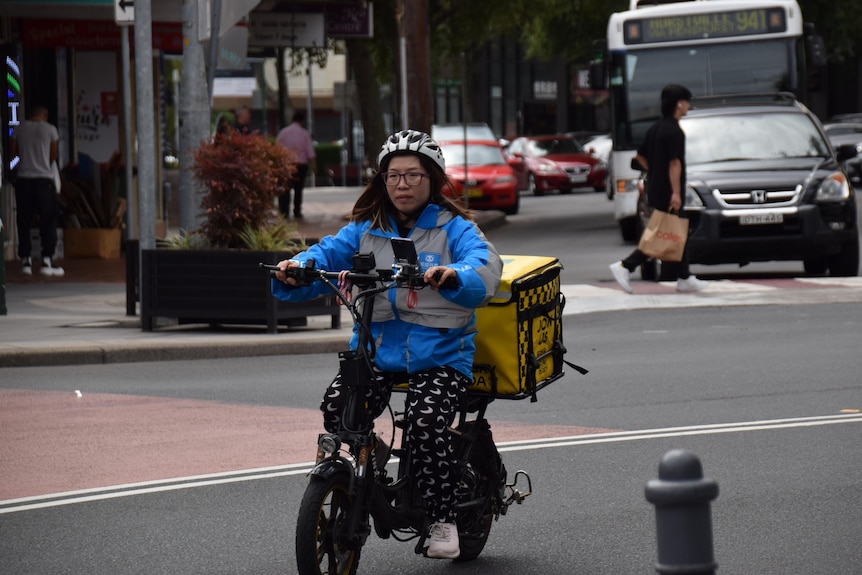 A woman riding a food delivery bike on a road.