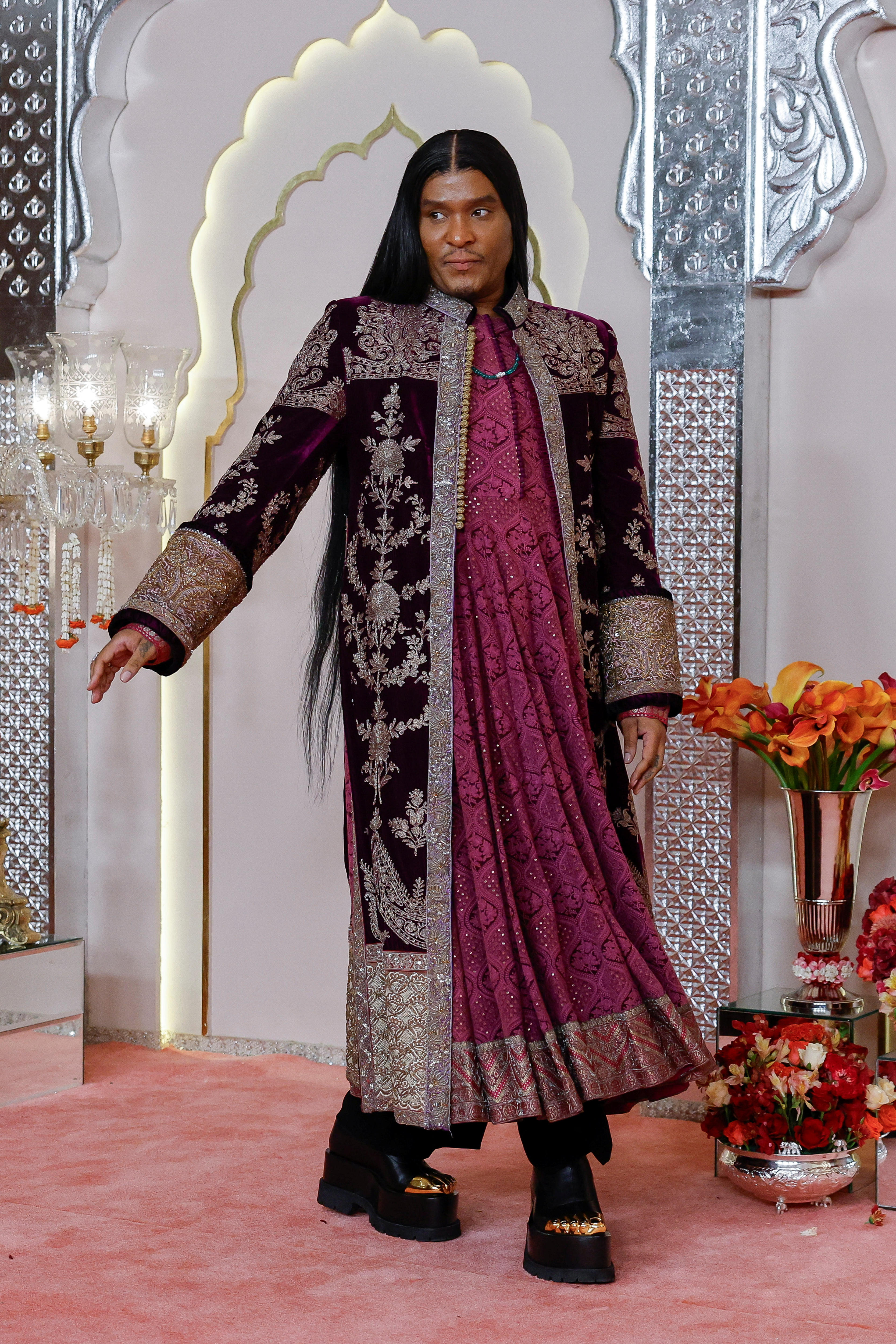 Law Roach wearing a long maroon tunic with a black and metallic embellished coat and thick platform shoes