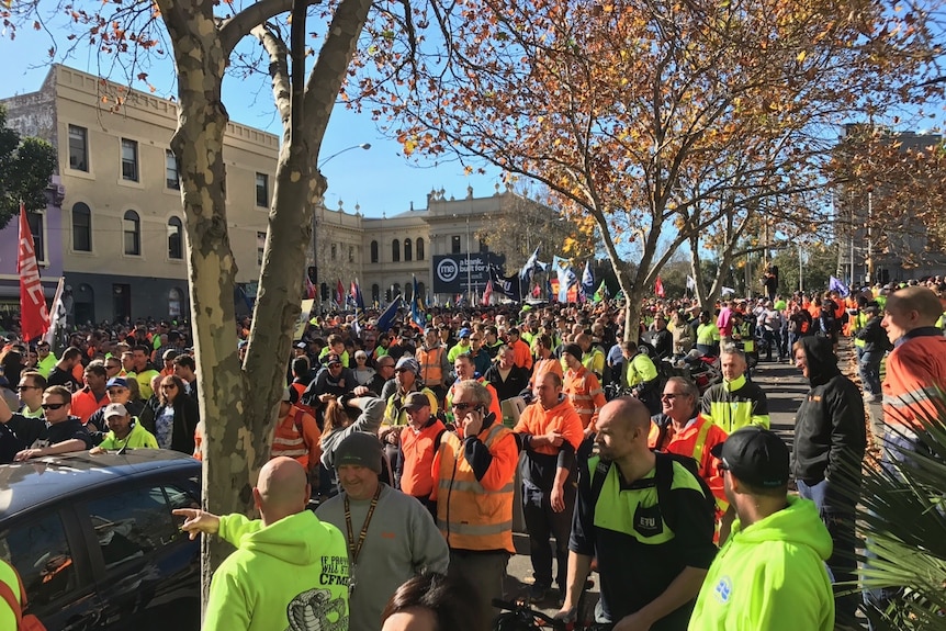 Hundreds of workers in high vis gear, holding signs march along a street in Melbourne's CBD.