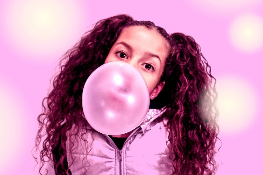 Young girl with long pigtails blows a bubblegum bubble.