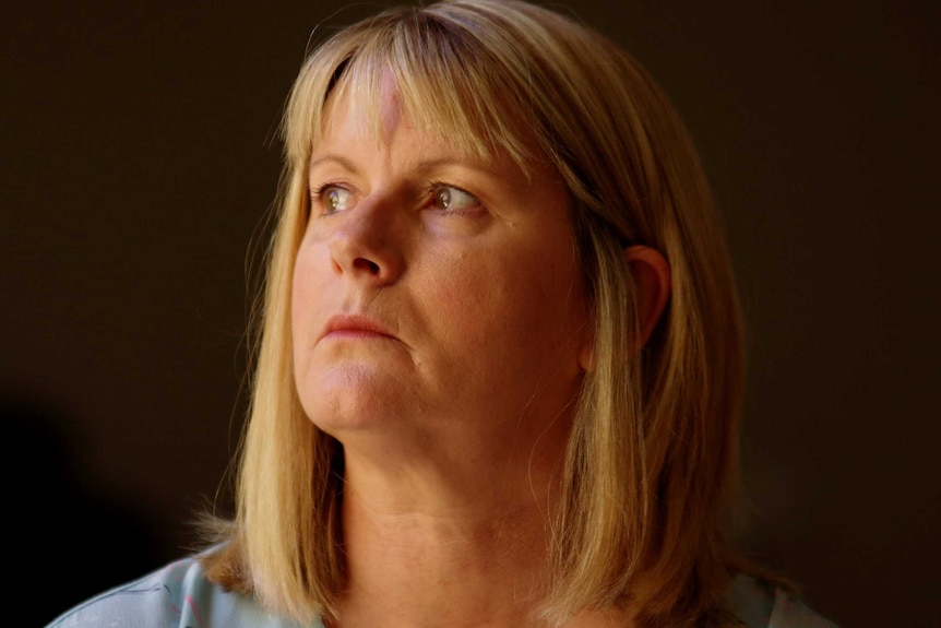 A head and shoulders portrait of a woman against a dark background looking to the left.