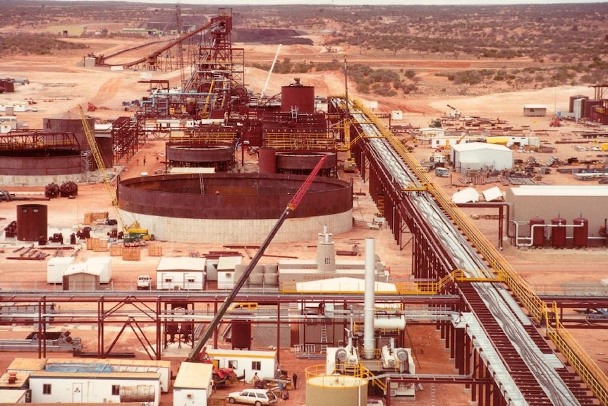 A large construction site in the middle of the desert is built using cranes, with an old panel van seen on site.