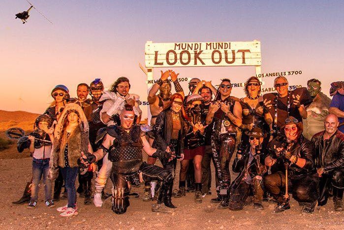 A group of people in Mad-Max themed costumes pose together under a sign that says 'Mundi Mundi Lookout'.