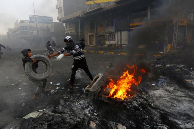 A boy and man burning tires in a street in Iraq.