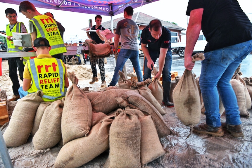 Men are seen lifting sandbags, while people wear fluro vests with the words "rapid relief team" on them.