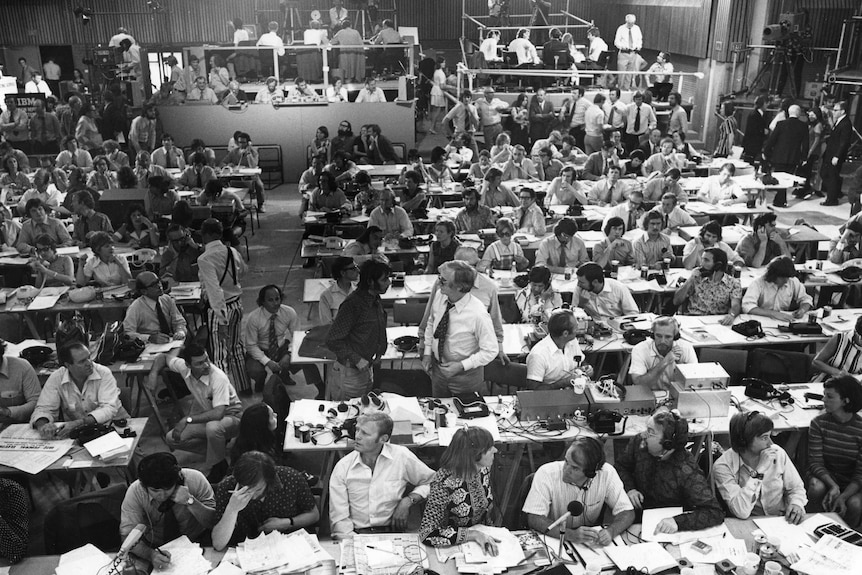 Wide shot of rows of desks with media set up and television panels in background.