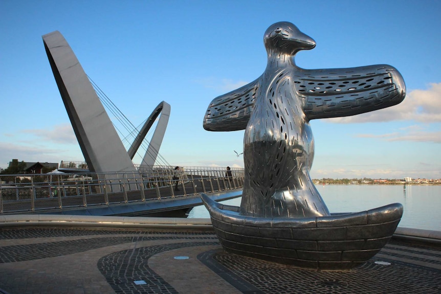 A huge aluminium sculpture sits next to a large steel bridge overlooking a river