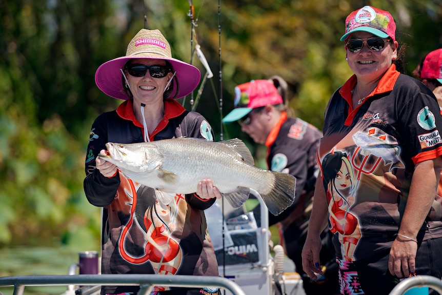 Woman in a straw hat holds a large live barramundi