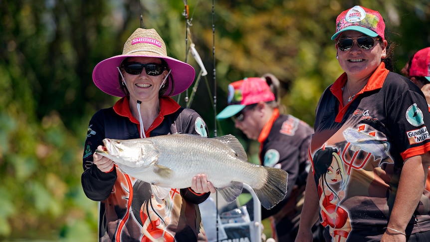Woman in a straw hat holds a large live barramundi